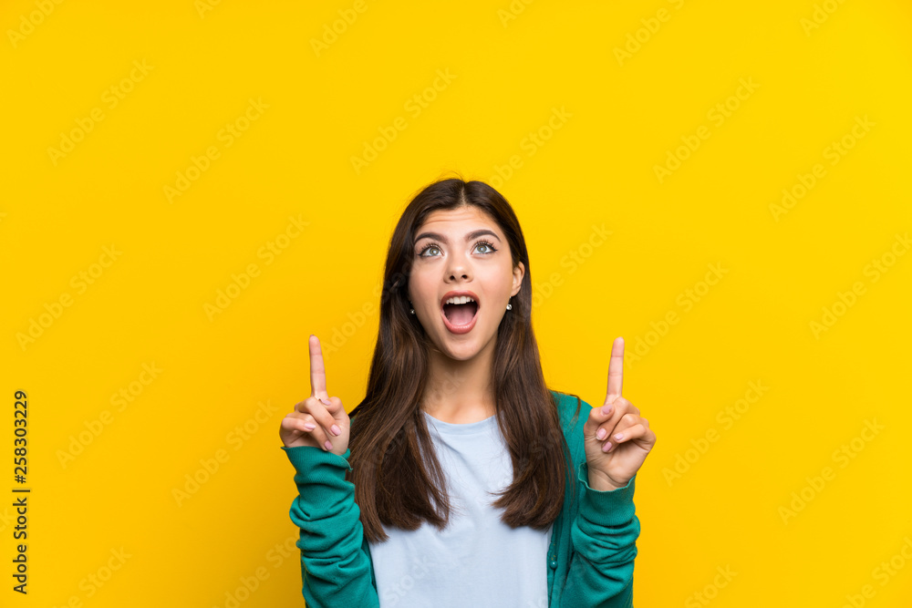 Teenager girl over yellow wall pointing with the index finger a great idea Teenager girl over yellow wall pointing with the index finger a great idea