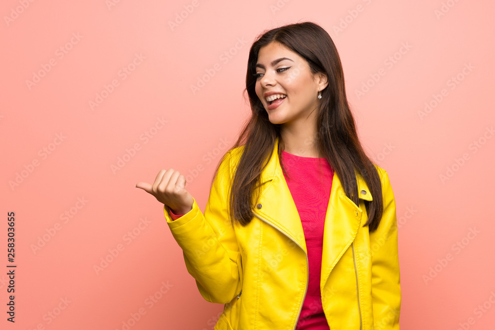 Teenager girl over pink wall pointing to the side to present a product Teenager girl over pink wall pointing to the side to present a product