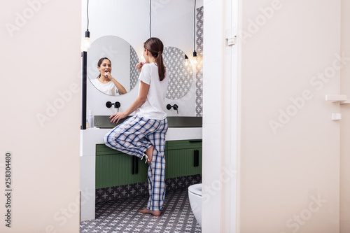 Woman with ponytail wearing baggy pajamas brushing teeth