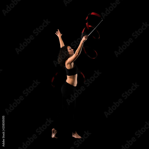 Woman doing rhythmic gymnastics with ribbon on black background © luismolinero