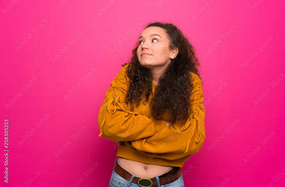 Teenager girl over pink wall making doubts gesture while lifting the shoulders Teenager girl over pink wall making doubts gesture while lifting the shoulders