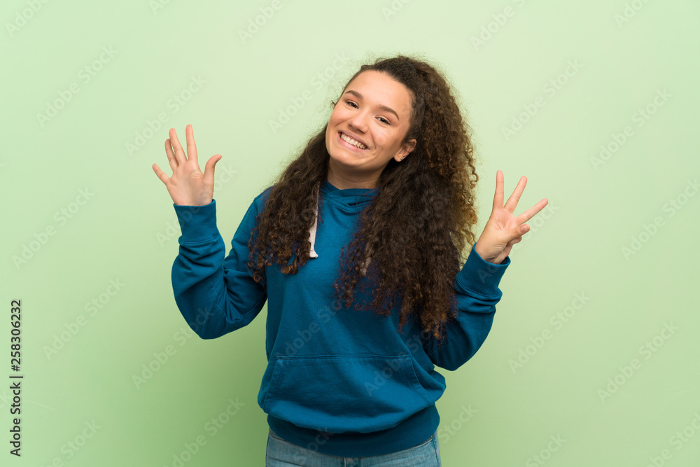 Teenager girl over green wall counting eight with fingers Teenager girl over green wall counting eight with fingers