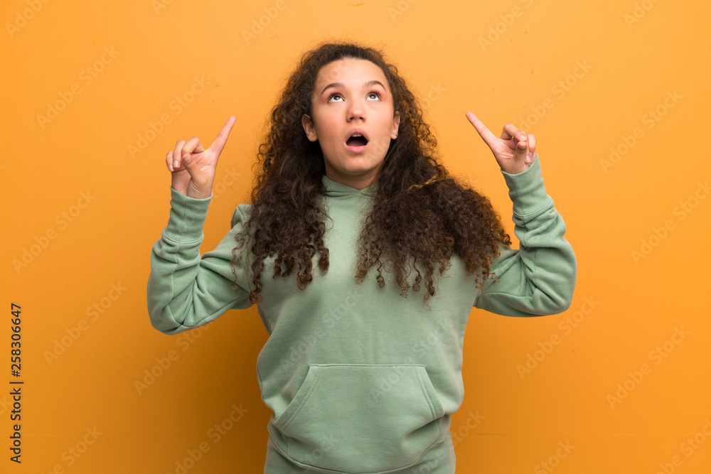 Teenager girl over ocher wall surprised and pointing up Teenager girl over ocher wall surprised and pointing up