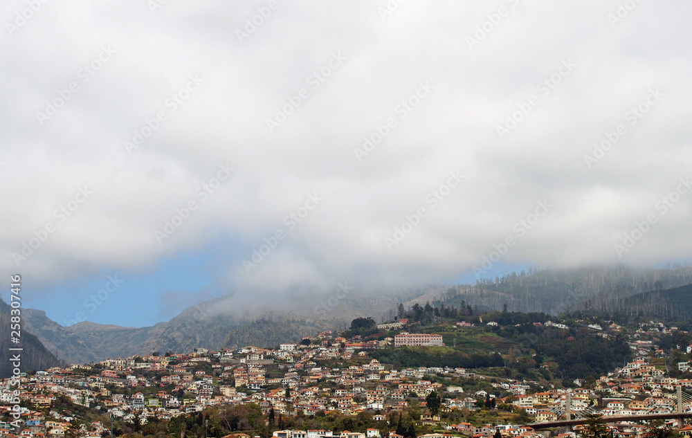 a panoramic view of funchal in madeira with houses between green hills and the mountains under white cloud