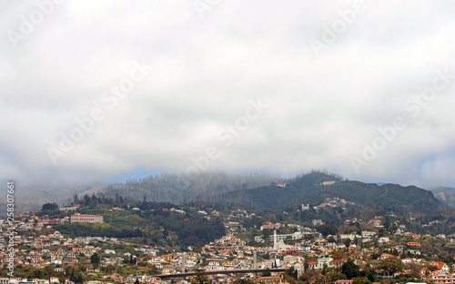 a panoramic view of the city of funchal with buildings and road bridge with mountains covered by white misty cloud © Philip J Openshaw 
