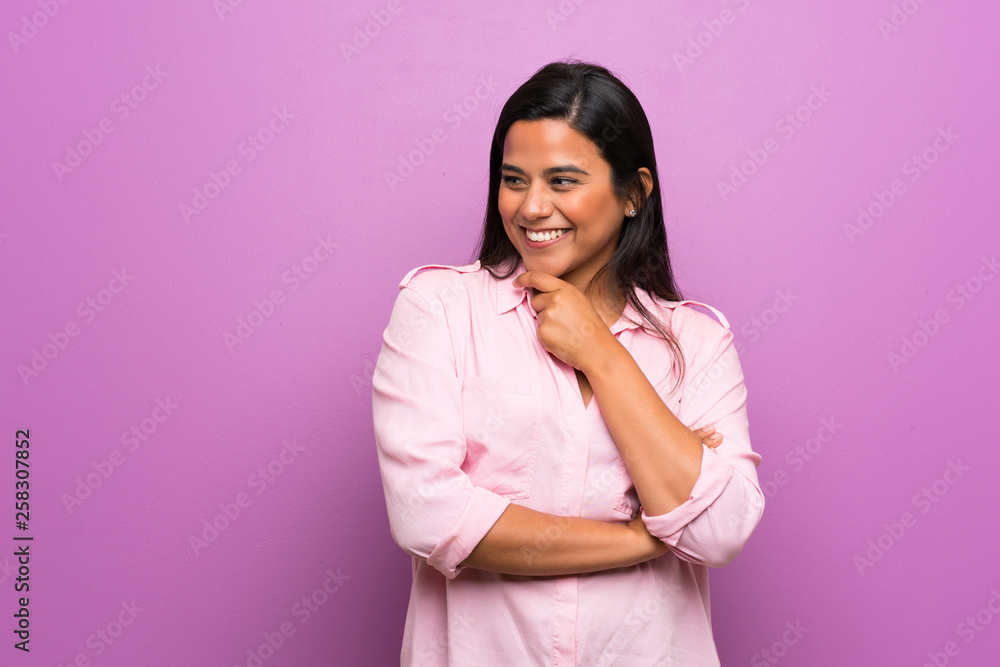 Young Colombian girl over purple wall looking to the side Young Colombian girl over purple wall looking to the side