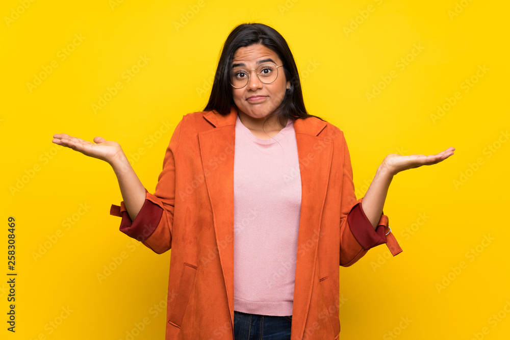 Young Colombian girl over yellow wall making unimportant gesture while lifting the shoulders Young Colombian girl over yellow wall making unimportant gesture while lifting the shoulders