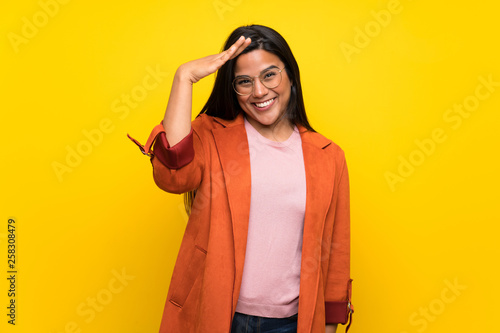 Young Colombian girl over yellow wall saluting with hand © luismolinero