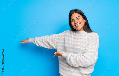 Young Colombian girl with sweater pointing back and presenting a product