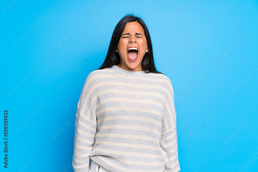 Fototapeta premium Young Colombian girl with sweater shouting to the front with mouth wide open
