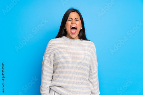 Young Colombian girl with sweater shouting to the front with mouth wide open