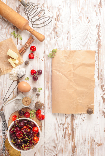 Cherry pie baking ingredients: fresh cherries, flour, egg, cinnamon, roller pin on a rustic white table. Background layout with free text space. Top view, flat lay style photo