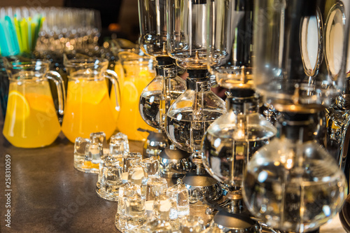 Elegant vacuum glass siphon and blurry orange drinks with slices of orange fruit inside big glass bowls in background. Drinks served on table ready for holiday celebration. Horizontal color photo.