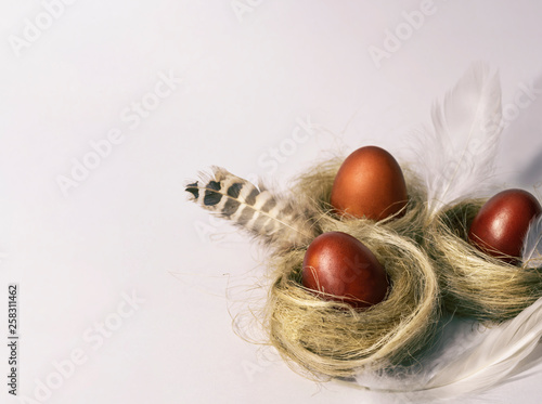 Three Easter red eggs in nests with white and variegated feathers.