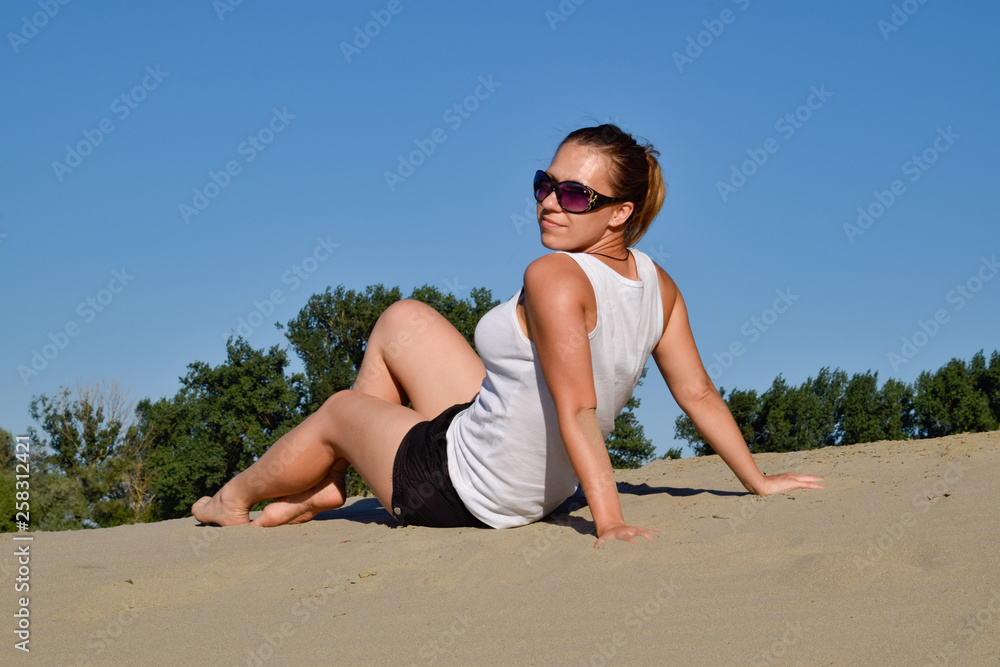 The girl in a white T-shirt on the sandy bank of the river The girl in a white T-shirt on the sandy bank of the river