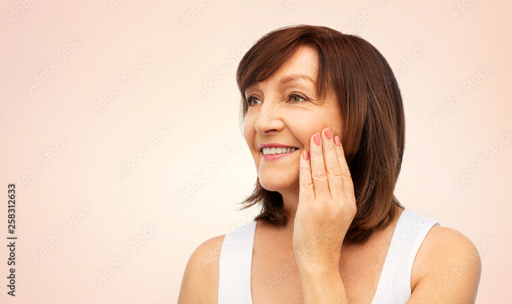 beauty, skin care and old people concept - portrait of smiling senior woman touching her face over beige background beauty, skin care and old people concept - portrait of smiling senior woman touching her face over beige background