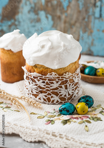 Two traditionally baked orthodox paskas with glace icing and bright blue and violet flowers on white woooden background with lace fabric. Easter cakes. Selective focus, copy space