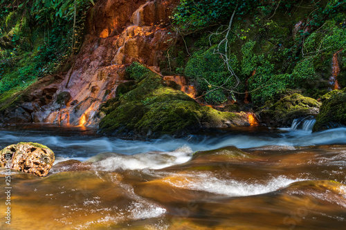 Long exposure of a river flowing through moss covered rocks shaping the landscape. Dodder river in Kiltipper Park, Dublin, Ireland.