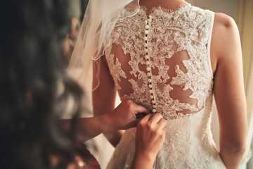 Bridesmaid helping bride fasten corset close-up and getting her dress, preparation concept in morning for wedding day.