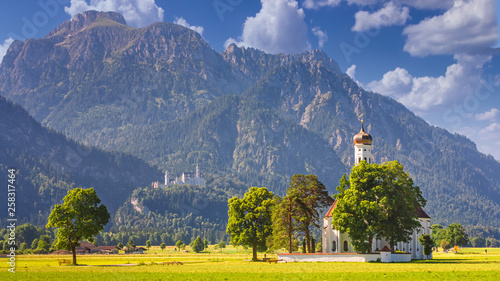 Bavarian landscape - view of the church of St. Coloman on the background of the Alpine mountains and Neuschwanstein Castle in summer day, Germany photo