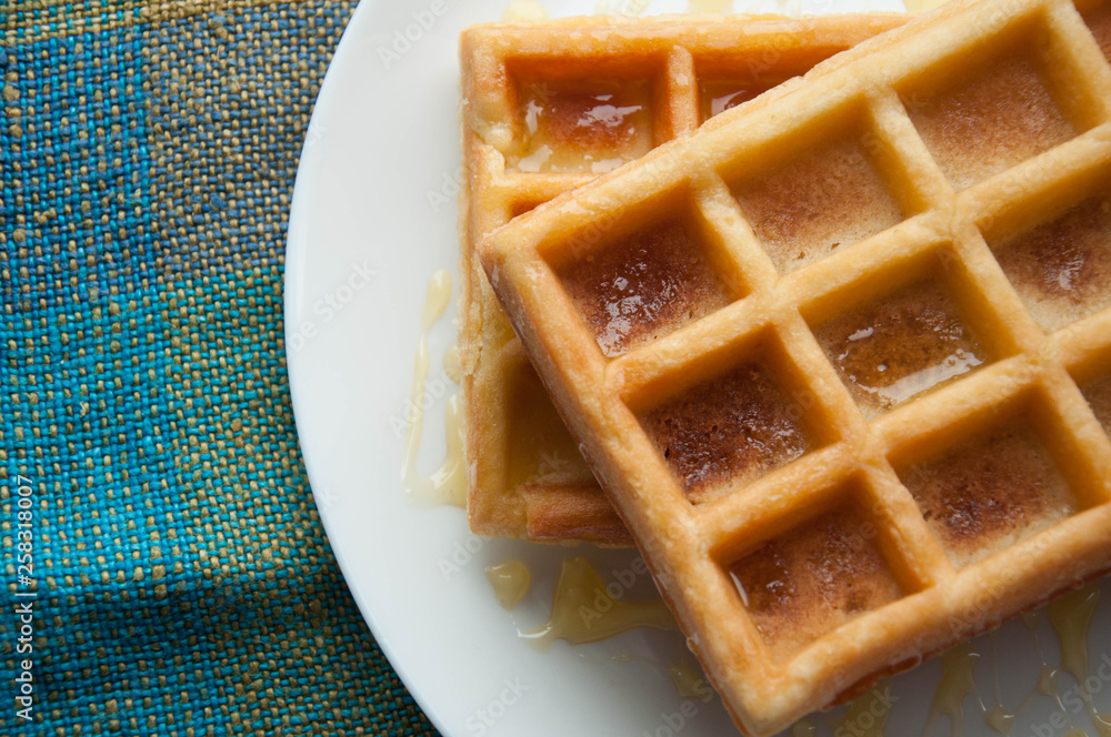 Belgian waffles on a white plate on the table. French or American breakfast. Vintage style. Sweet food. Belgian waffles on a white plate on the table. French or American breakfast. Vintage style. Sweet food.