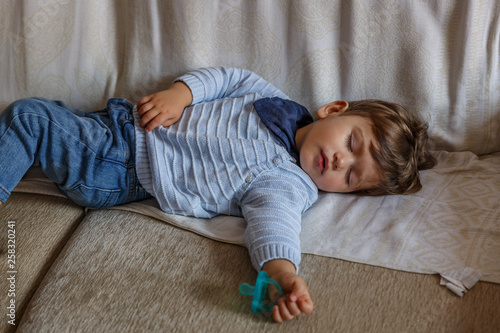 Tableau sur toile A tender little toddler boy dressed in blue, is resting peacefully on the sofa i