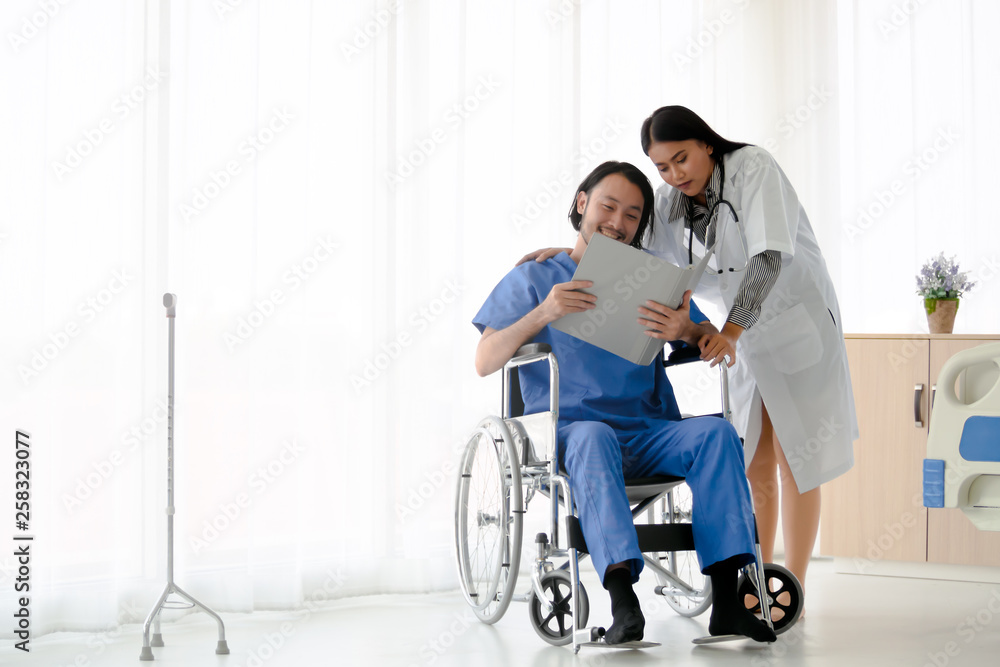 Female doctor take care of smiling asian male patient who sitting on wheelchair with document file folder. The young man recover from illness. Healthcare and medical concept. Female doctor take care of smiling asian male patient who sitting on wheelchair with document file folder. The young man recover from illness. Healthcare and medical concept.