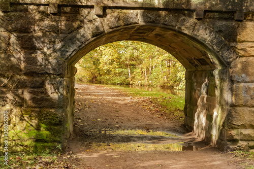 Fototapeta Naklejka Na Ścianę i Meble -  Canal towpath stretches under the stone arch of bridge