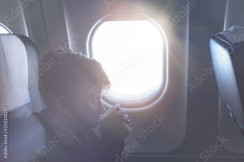 A boy drinking from paper cup sitting near airplane window during air flight. Food served on board
