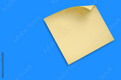 One blank square yellow sticker with curved corner attached on blue table in office or fridge in home. Top view. Copy space for your text. Business or education concept