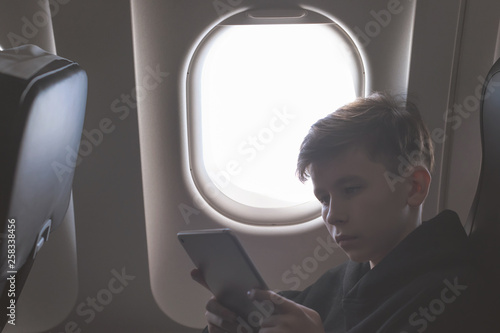 Caucasian boy fasten seat belt and using tablet pc and taking picture during air flight. Safety travel with kid. concept