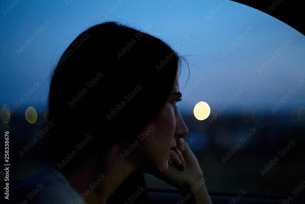 The woman sit in a car on the city lights background. evening night time The woman sit in a car on the city lights background. evening night time