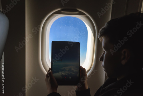 Caucasian boy fasten seat belt and using tablet pc and taking picture during air flight.  Safety travel with kid. concept photo