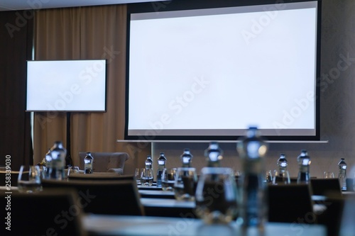 Conference room with two blank white screens. Bottles out of focus.