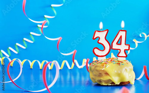 Birthday of thirty four years. Cupcake with white burning candle in the form of number 34. Vivid blue background with copy space photo