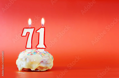 Seventy one years birthday. Cupcake with white burning candle in the form of number 71. Vivid red background with copy space