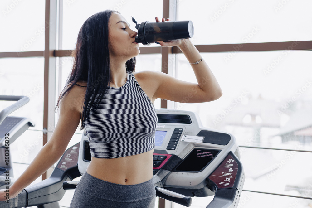 Girl in the gym are trained on treadmill and drink water Girl in the gym are trained on treadmill and drink water