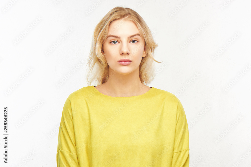 Portrait of beautiful serious European girl on white background Isolated. Attractive blonde business woman in yellow clothes looks into the camera busily