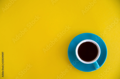 Blue cup of coffee stands on a yellow background. Morning breakfast, business.