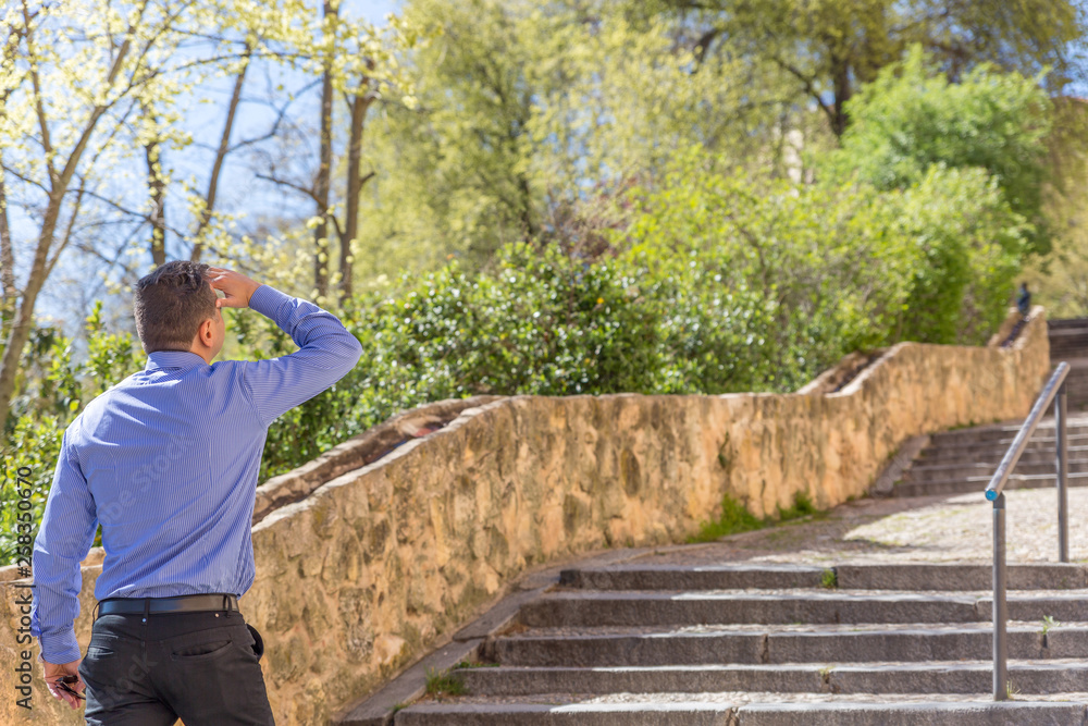 Fototapeta premium An elegant man in a blue shirt looks attentively on a street uphill with stairs