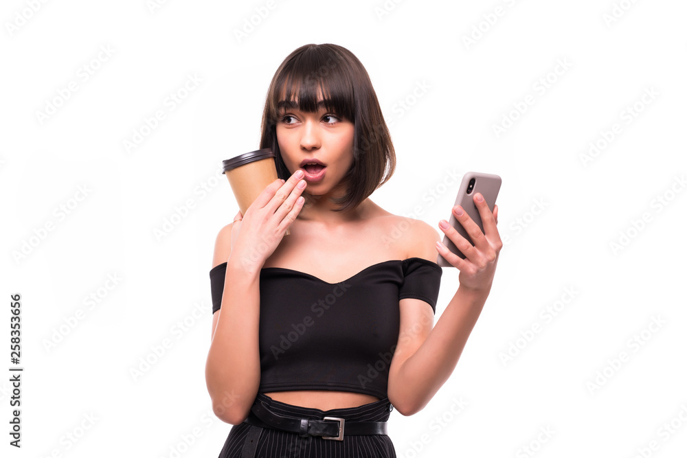 Portrait of shocked young woman typing by mobile phone drinking coffee posing isolated over grey wall background Portrait of shocked young woman typing by mobile phone drinking coffee posing isolated over grey wall background