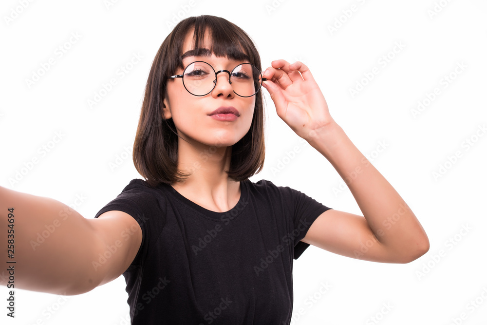 Portrait of a smiling cute woman in glasses making selfie photo on smartphone on a white background.