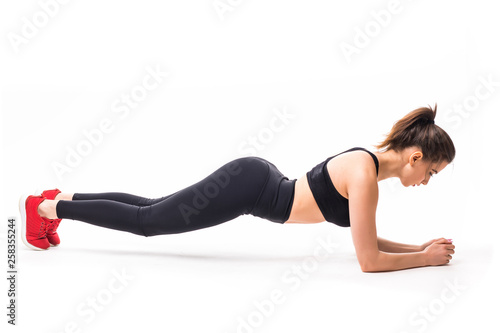 Concentrated beautiful fitness girl in sportwear exercising doing a plank isolated over white background © dianagrytsku