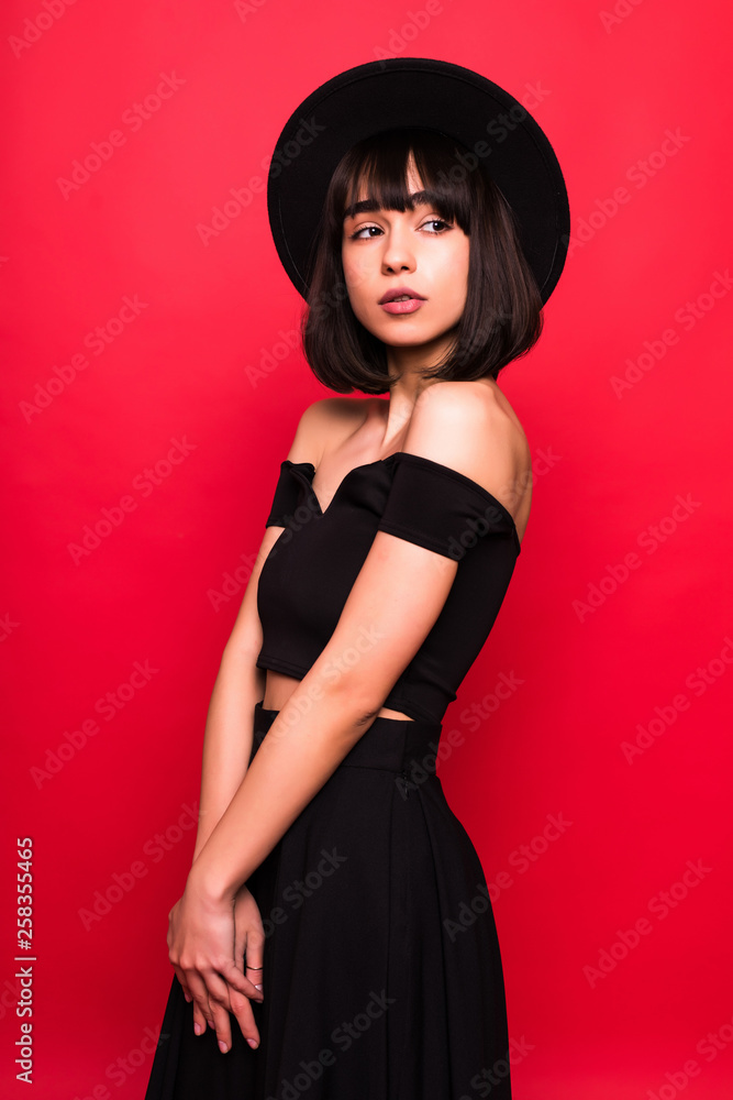 Young brunette woman in fluppy hat and black clothes on red background Young brunette woman in fluppy hat and black clothes on red background