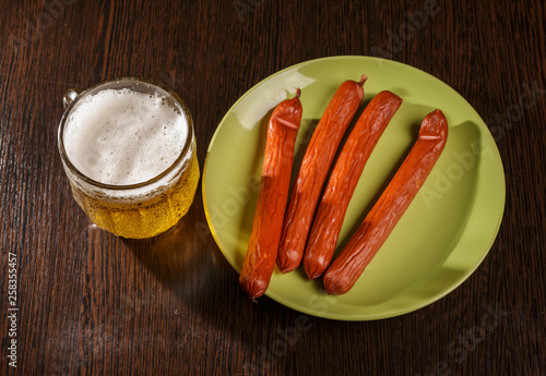 A small glass of beer and smoked sausage on the table.