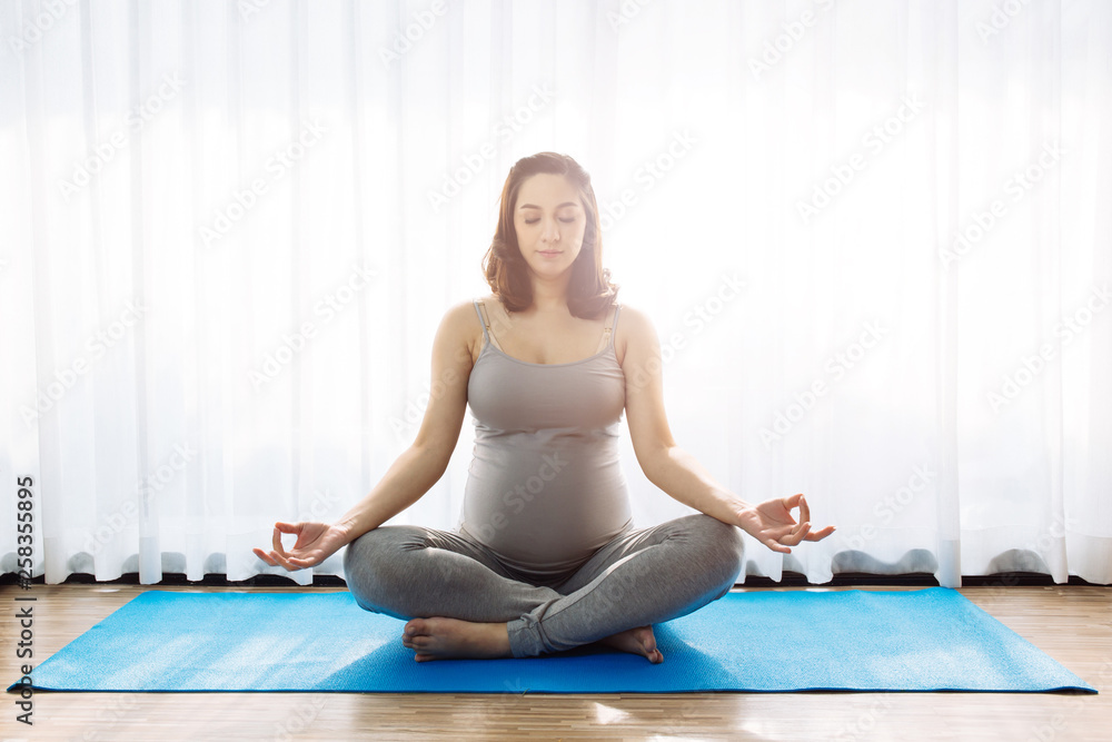 Young attractive pregnant woman practicing yoga over the window view in the morning with copy space Young attractive pregnant woman practicing yoga over the window view in the morning with copy space