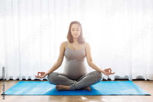 Young attractive pregnant woman practicing yoga over the window view in the morning with copy space