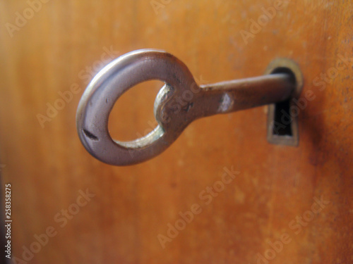 An old antique key reveals secrets under lock and key. The round key sticks out of the keyhole and is ready to open the door.