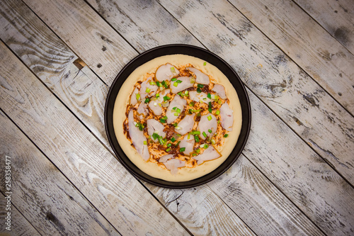 Round pizza dough is in the pan. The process of cooking pizza, stacking ingredients on the dough.