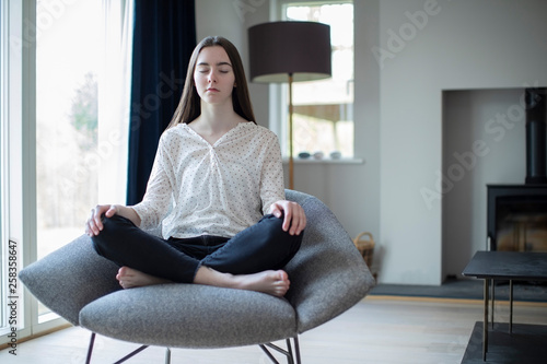 Peaceful Teenage Girl Meditating Sitting In Chair At Home